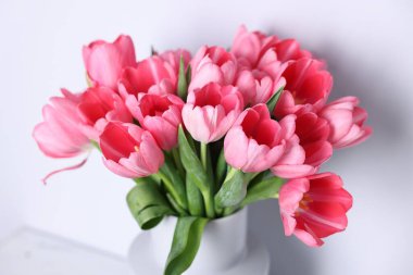 Açık gri duvarın yanında vazoda pembe laleler var.