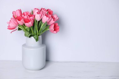 Gri duvarın yakınındaki açık mermer masada vazoda duran pembe lale buketi. Metin için boşluk