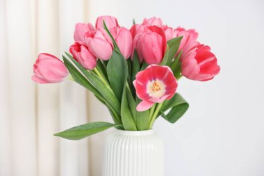 Beyaz duvarın yanındaki vazoda pembe laleler, yakın plan.