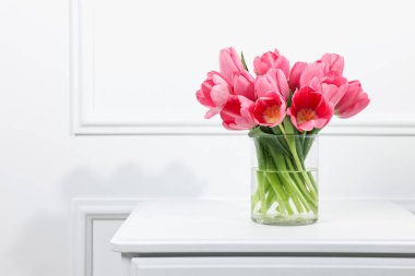 Güzel pembe laleler vazonun içinde beyaz şifoniyer üzerinde, metin için yer var.