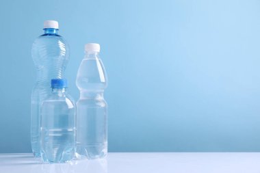 Beyaz masada açık mavi arka planda farklı boyutlarda su şişeleri var. Metin için boşluk
