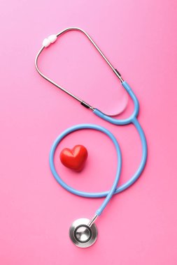 Pembe arka planda steteskop ve kırmızı kalp, düz yatıyordu.