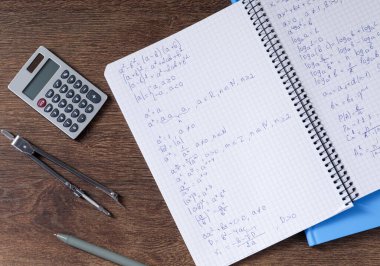 Ev ödevi. Matematik formülleri ve ahşap masa üzerindeki farklı kırtasiyeli defter.