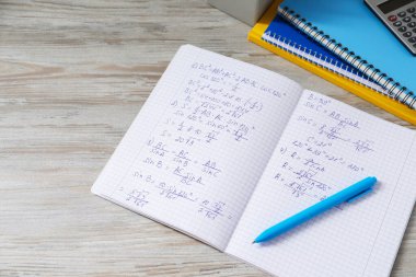 Ev ödevi. Matematik formülleri ve açık gri ahşap masa üzerindeki farklı kırtasiyeli defter.