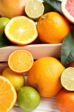 Beyaz ahşap masada sandıkta farklı olgun narenciye meyveleri, yakın plan.