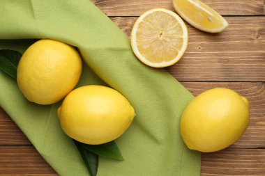 Taze limon meyveleri ve ahşap masada yeşil yapraklar, düz uzanmış.