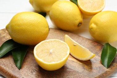 Taze limon meyveleri ve yeşil yapraklar beyaz masada, yakın plan.