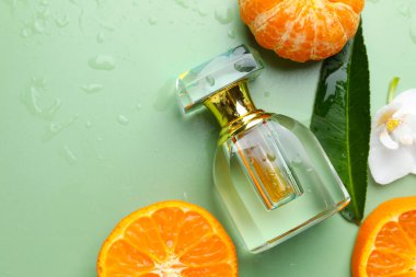 Islak parfüm şişesi, çiçek ve açık yeşil arka planda mandalina. Metin için boşluk