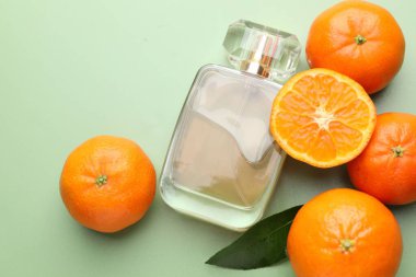 Açık yeşil arka planda bir şişe parfüm ve mandalina. Metin için boşluk