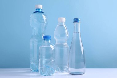 Açık mavi arka planda beyaz masada farklı boyutlarda su şişeleri