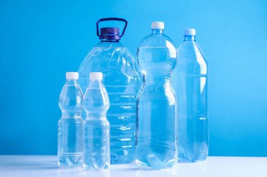 Açık mavi arka planda beyaz masada farklı boyutlarda su şişeleri