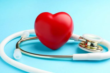 Açık mavi arka planda beyaz steteskop ve kalp modeli, yakın plan.