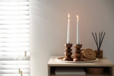 İçinde yanan mumlar ve ahşap masa üzerinde sazlık dağıtıcı bulunan zarif şamdanlar.