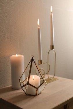 Bej duvarın yanındaki ahşap masada şamdanların içinde yanan güzel mumlar.