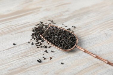 Tahta masada bronz kepçeyle kurutulmuş siyah çay yaprakları, yakın plan.