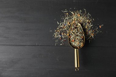 Siyah ahşap masa üzerinde kurutulmuş bitki çayı yapraklarıyla kepçe, üst manzara. Metin için boşluk