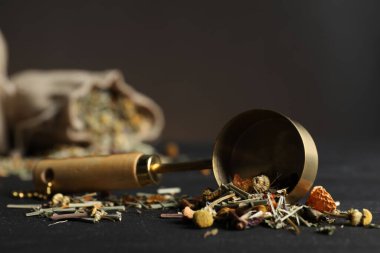 Kurutulmuş bitki çayı yaprakları ve siyah masaya kepçe, yakın plan.