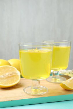 Tatlı kaselerinde leziz sarı jöle ve açık mavi ahşap masada limonlar, yakın plan.