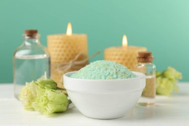 Kasede yeşil deniz tuzu, yanan mumlar ve çiçekler beyaz ahşap masada turkuaz arka planda, yakın plan