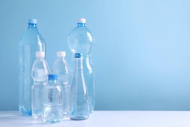 Beyaz masada açık mavi arka planda farklı boyutlarda su şişeleri var. Metin için boşluk