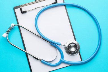 Açık mavi arkaplanda steteskop ve pano, üst görünüm