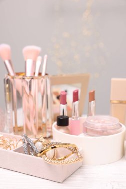 Makyaj ürünleri tutacaklarda ve mücevher kutusu açık ahşap masada gri arka planda, yakın plan. Bokeh etkisi