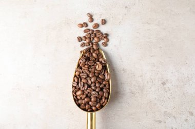 Kahve çekirdeği yığını ve açık gri desenli masada metal kepçe.