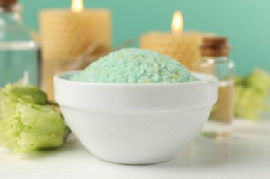 Kasede yeşil deniz tuzu, yanan mumlar ve çiçekler beyaz ahşap masada turkuaz arka planda, yakın plan