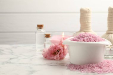 Kasede pembe deniz tuzu, bitkisel torbalar, yanan mumlar ve beyaz mermer masada çiçek, yakın plan.
