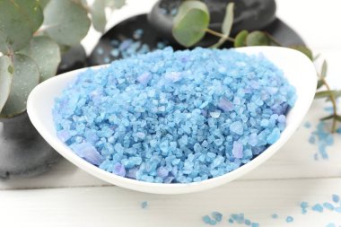 Kasedeki mavi deniz tuzu, spa taşları ve okaliptüs dalları beyaz ahşap masada, yakın plan.