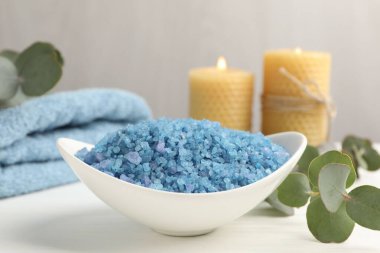 Kasede mavi deniz tuzu, yanan mumlar, havlular ve okaliptüs dalları beyaz ahşap masada, yakın plan.