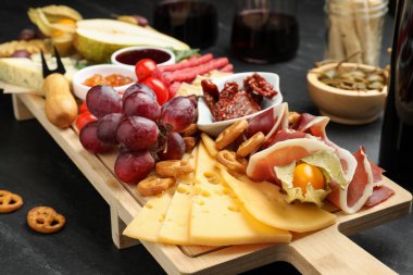 Siyah masada farklı atıştırmalıklar ve şaraplar olan şarküteri tahtası, yakın plan.