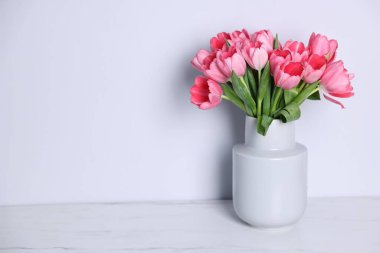 Gri duvarın yakınındaki açık mermer masada vazoda duran pembe lale buketi. Metin için boşluk