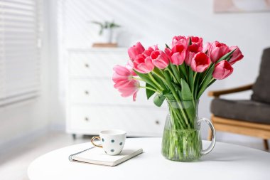 Vazoda pembe lale buketi, beyaz masada not defteri ve fincan.