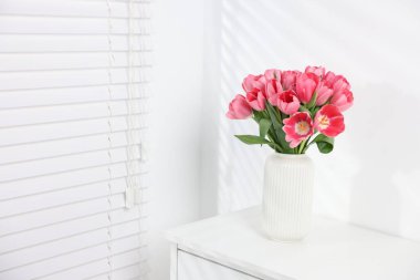 Beyaz duvarın yanındaki çekmece çekmecesinde vazoda duran pembe laleler. Metin için boşluk