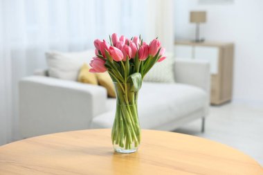 İçerideki ahşap masada vazoda pembe laleler, yakın plan.