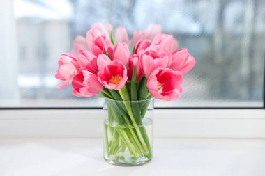 Pencere kenarındaki vazoda güzel pembe laleler.