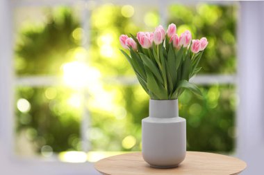 Pencere kenarındaki masada vazoda duran pembe laleler.