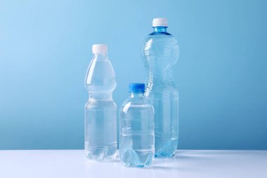 Açık mavi arka planda beyaz masada farklı boyutlarda su şişeleri