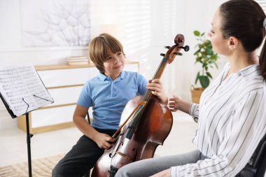 Küçük çocuk içeride müzik öğretmeniyle viyolonsel çalmayı öğreniyor.