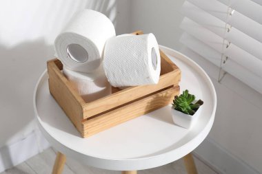 Tuvalet kağıdı ruloları sandıkta ve çiçekli dekor beyaz masa üzerinde kapalı pencere, yakın çekim