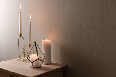 Bej duvarın yanındaki ahşap masada şamdanların içinde yanan mumlar. Metin için boşluk