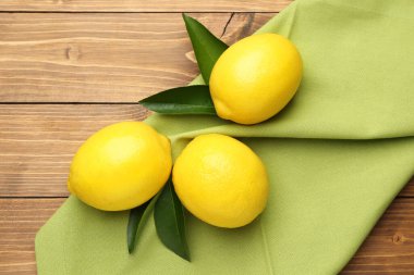 Taze limon meyveleri ve ahşap masada yeşil yapraklar, düz uzanmış.
