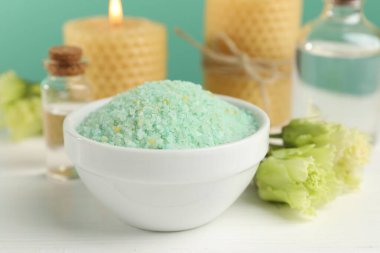 Kasede yeşil deniz tuzu, yanan mumlar ve çiçekler beyaz ahşap masada turkuaz arka planda, yakın plan