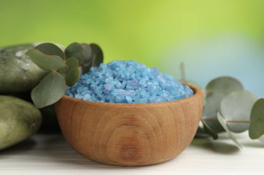 Mavi deniz tuzu kasede, taşlar ve okaliptüs yaprakları beyaz ahşap masada bulanık yeşil arka planda, yakın plan