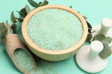 Kase içinde yeşil deniz tuzu, kepçe, masaj taşları ve turkuaz üzerinde okaliptüs dalları, yakın çekim.