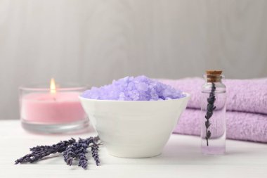 Mor deniz tuzu kasede, lavanta çiçekleri, yanan mum, beyaz ahşap masada gerekli yağ ve havlular, yakın plan.