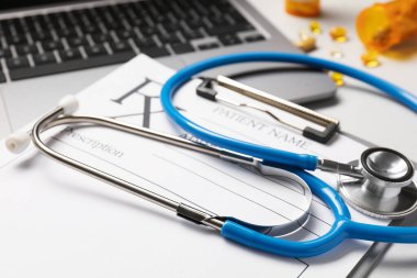 Açık gri masada steteskop, laptop ve pano, yakın plan.