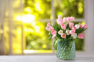 Pencere kenarında vazoda pembe ve beyaz laleler.