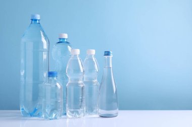Beyaz masada açık mavi arka planda farklı boyutlarda su şişeleri var. Metin için boşluk
